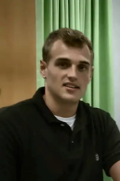 Nathanael as a Pensacola Christian College nursing student in a black polo, seated in the nursing skills lab during IV practice.