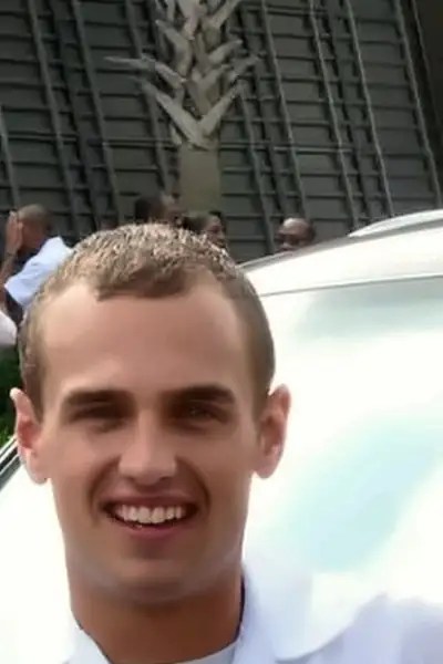 Nathanael smiling outdoors in his white nursing uniform with his new nursing pin on pinning day.