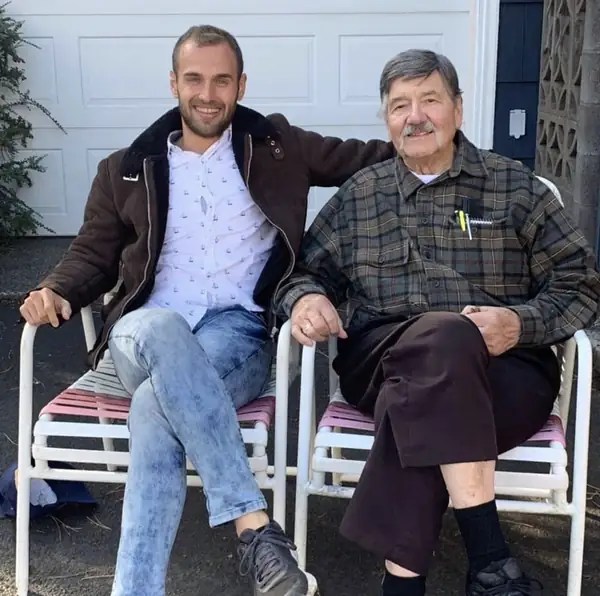 Nathanael and his grandfather, Kenneth Smith, sitting side by side in lawn chairs outside a white garage, both smiling, Nathanael's arm around his grandpa.